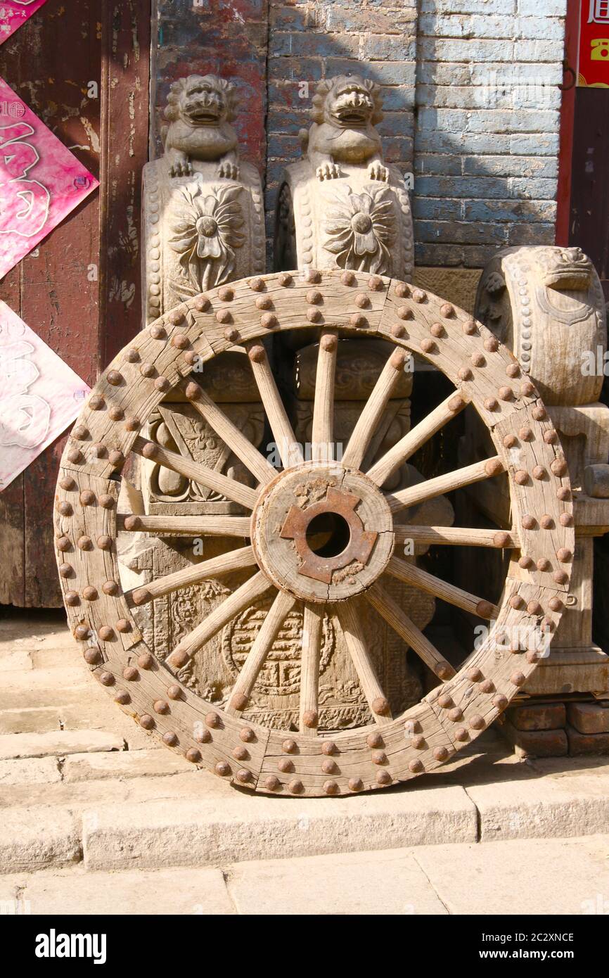 Image showing an antique metal studded wooden wheel and some sculptures and furniture outside an antique  shop in the ancient town of Zhou Cun, Stock Photo