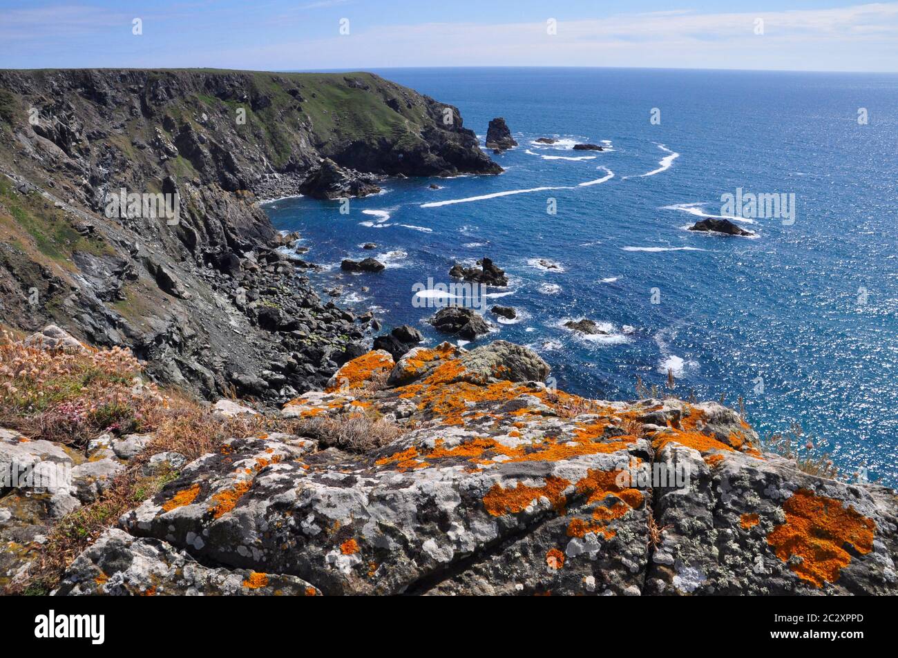 Crumbling Cliffs above a calm blue sea on the coast of the Lizard peninsula viewed from lichen covered granite rocks.Cornwall, England,UK Stock Photo
