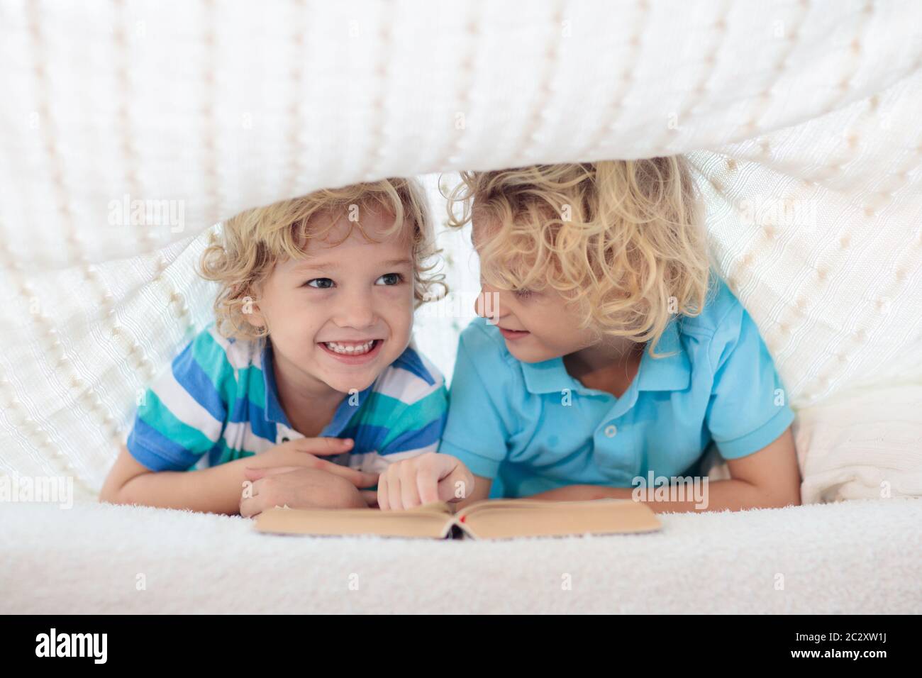 Child Reading Book In Bed Under Knitted Blanket. Two Brothers Playing ...