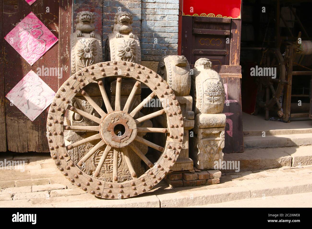 Image showing an antique metal studded wooden wheel and some sculptures and furniture outside an antique shop, Zhou Cun, Shandong Province, China Stock Photo
