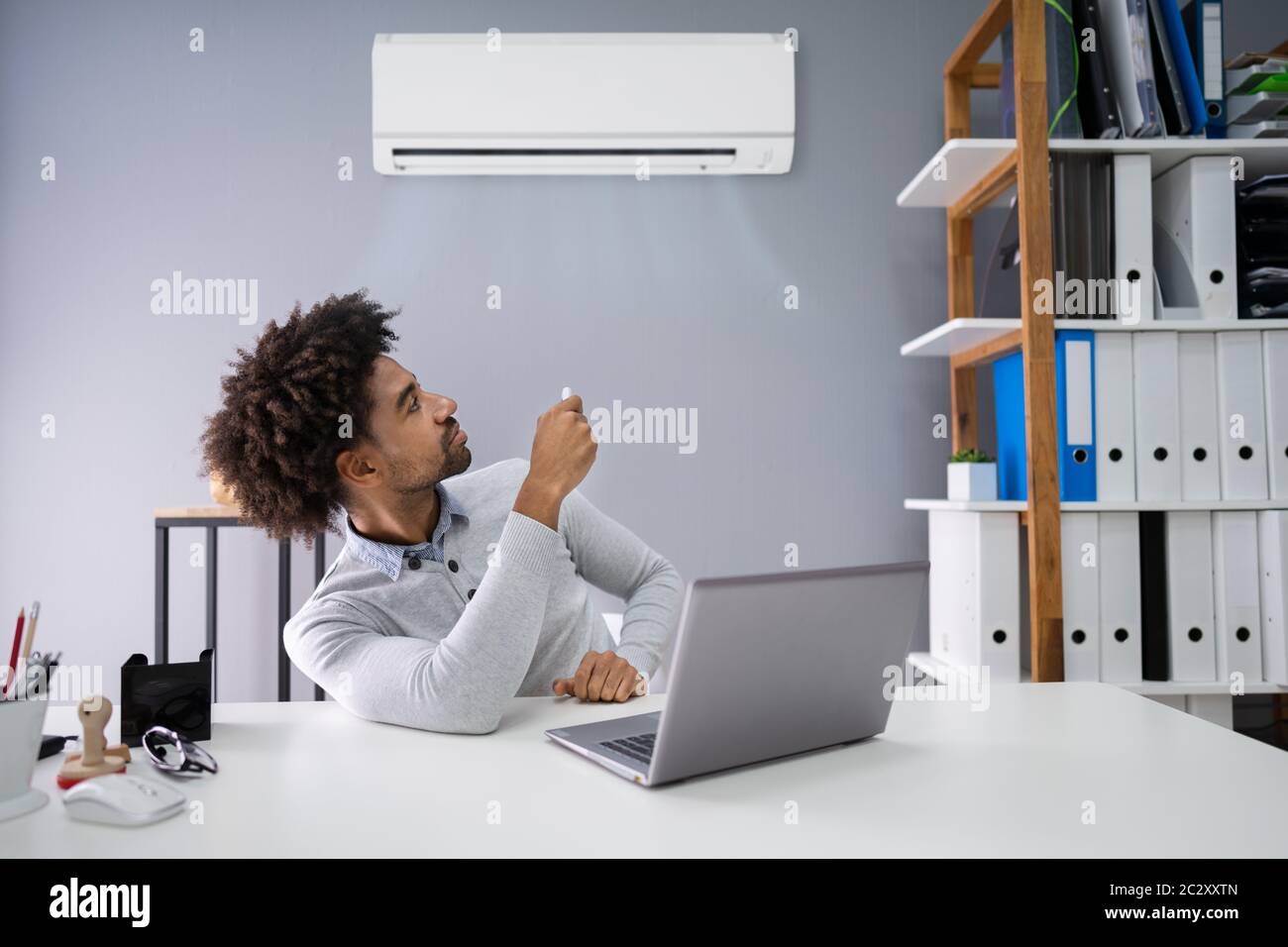 Young Businessman Operating Air Conditioner With Remote Controller In Office Stock Photo