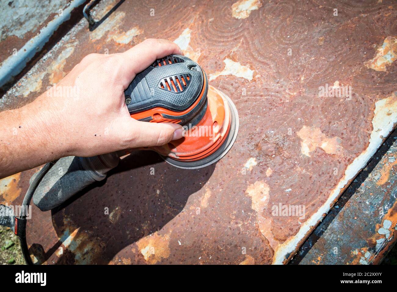 Man's hand operates a disc/orbital sander, to remove paint and rust from metal doors Stock Photo