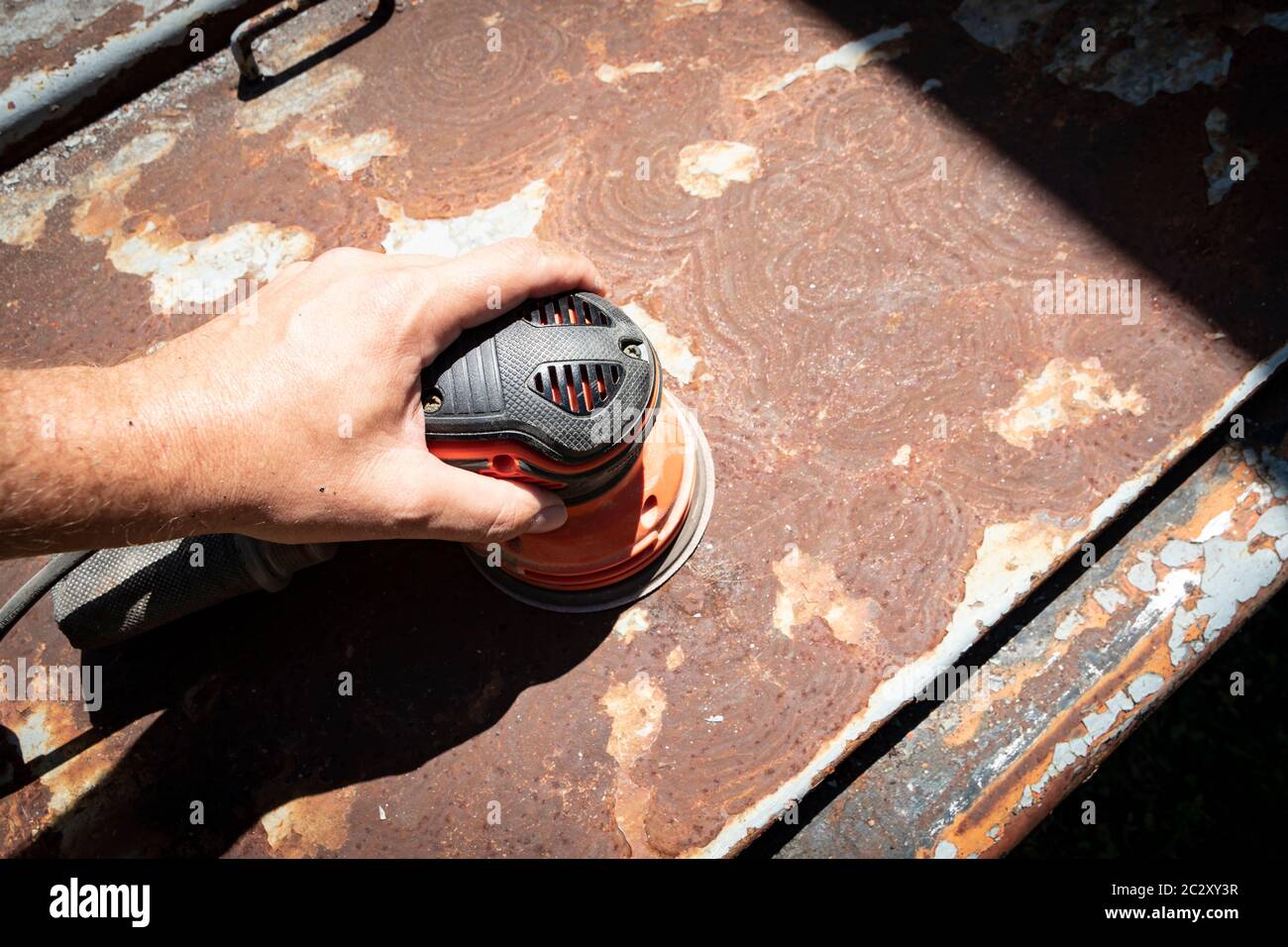 Man's hand operates a disc/orbital sander, to remove paint and rust from metal doors Stock Photo