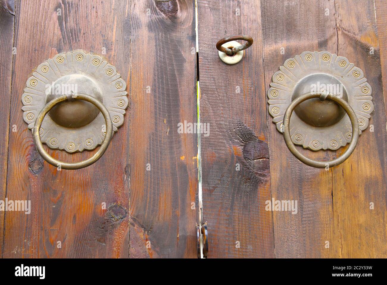 Image showing wooden double doors with a pair of stylized flower-shaped brass door knockers. Horizontal orientation. Stock Photo