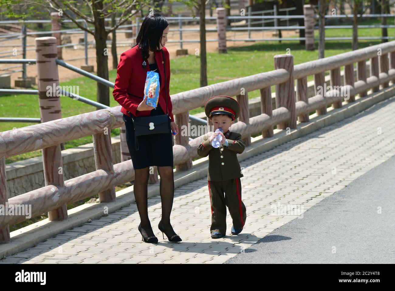 Pyongyang, North Korea - May 1, 2019: Young mom and her little son, dressed in the uniform of the Korean People’s Army, are walking on Pyongyang stree Stock Photo