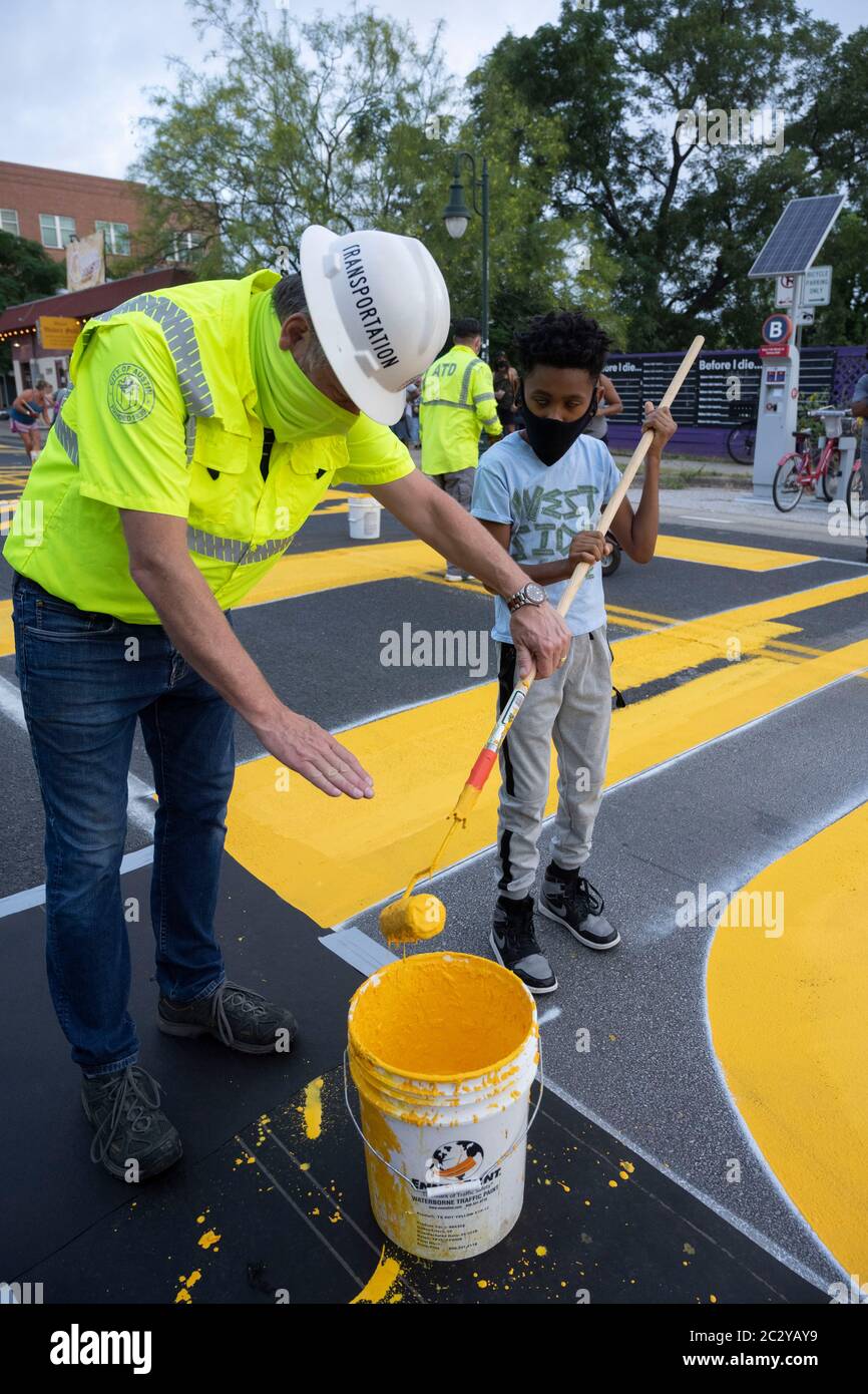 City of Austin Transportation Director Robert Spillar teaches Tobias Jackson-Woods how to use a paint roller as artists paint a mural on east 11th Street near downtown Austin that says 'Black Artists Matter,' two days after the group painted 'Black Austin Matters' in large yellow letters on Congress Avenue in the heart of downtown. Stock Photo