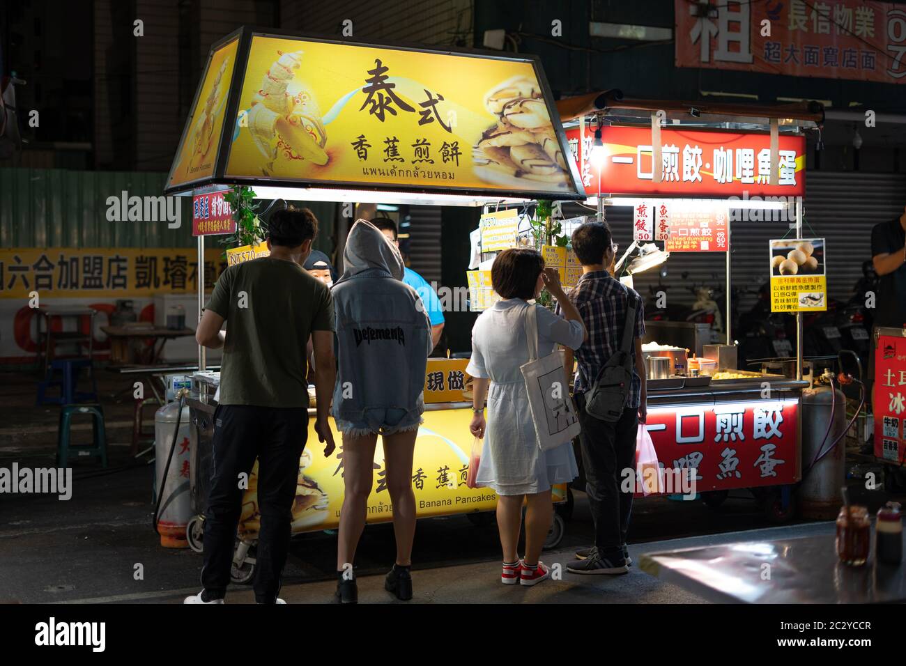 People waiting in front of a street food vendor for some Thai Style baked Bananas with honey at a local night market Stock Photo