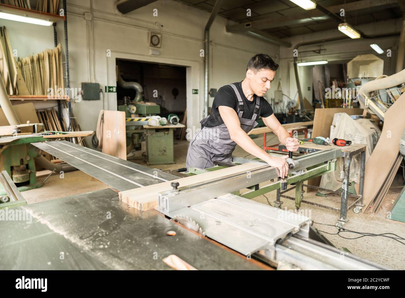 Worker cutting on a sliding table saw in a factory. Mid shot. Stock Photo