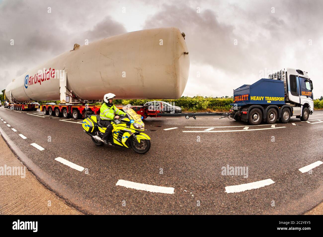 Shenstone, Staffordshire, UK. 18th June, 2020. A supersize oxygen tank - 40m long and 6.5m wide - is on its fourth day or transport across the midlands. Two cabs pulling and pushing, 156 wheels, four drivers, and many police and BT engineers and tree cutters are involved, as the enormous load goes from Cheshire to north Warwickshire. An 8mm fisheye lens just about managed to capture the scene. Credit: Peter Lopeman/Alamy Live News Stock Photo