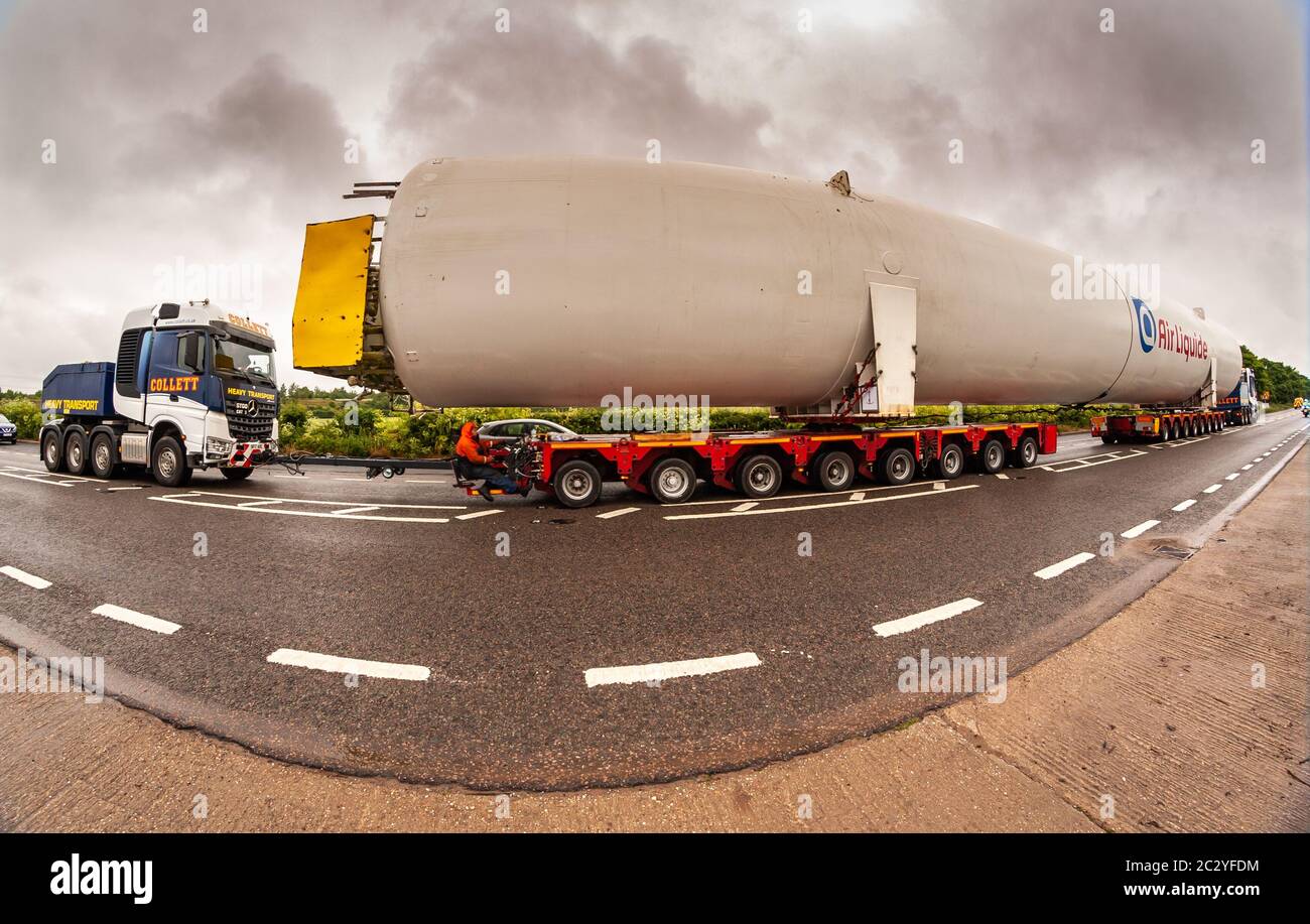 Shenstone, Staffordshire, UK. 18th June, 2020. A supersize oxygen tank - 40m long and 6.5m wide - is on its fourth day or transport across the midlands. Two cabs pulling and pushing, 156 wheels, four drivers, and many police and BT engineers and tree cutters are involved, as the enormous load goes from Cheshire to north Warwickshire. An 8mm fisheye lens just about managed to capture the scene. Credit: Peter Lopeman/Alamy Live News Stock Photo