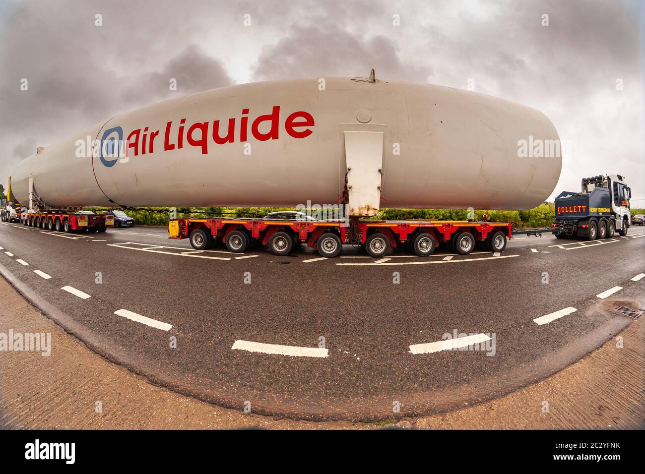 Shenstone, Staffordshire, UK. 18th June, 2020. A supersize oxygen tank - 40m long and 6.5m wide - is on its fourth day or transport across the midlands. Two cabs pulling and pushing, 156 wheels, four drivers, and many police and BT engineers and tree cutters are involved, as the enormous load goes from Cheshire to north Warwickshire. An 8mm fisheye lens just about managed to capture the scene. Credit: Peter Lopeman/Alamy Live News Stock Photo