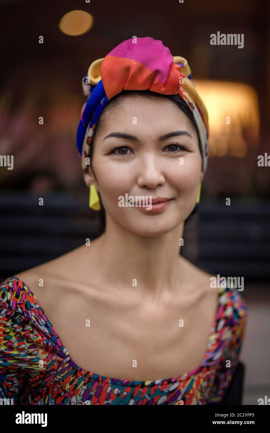 Girl of oriental ethnicity with a scarf on her head, portrait against the background of a window with a table lamp Stock Photo
