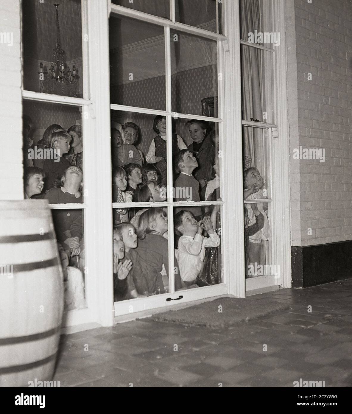 1960s, historical, a grouo of excited young children at a party in a house peering out the windows at the back of house to the patio ouside to try and see the surprise, England, UK. Stock Photo