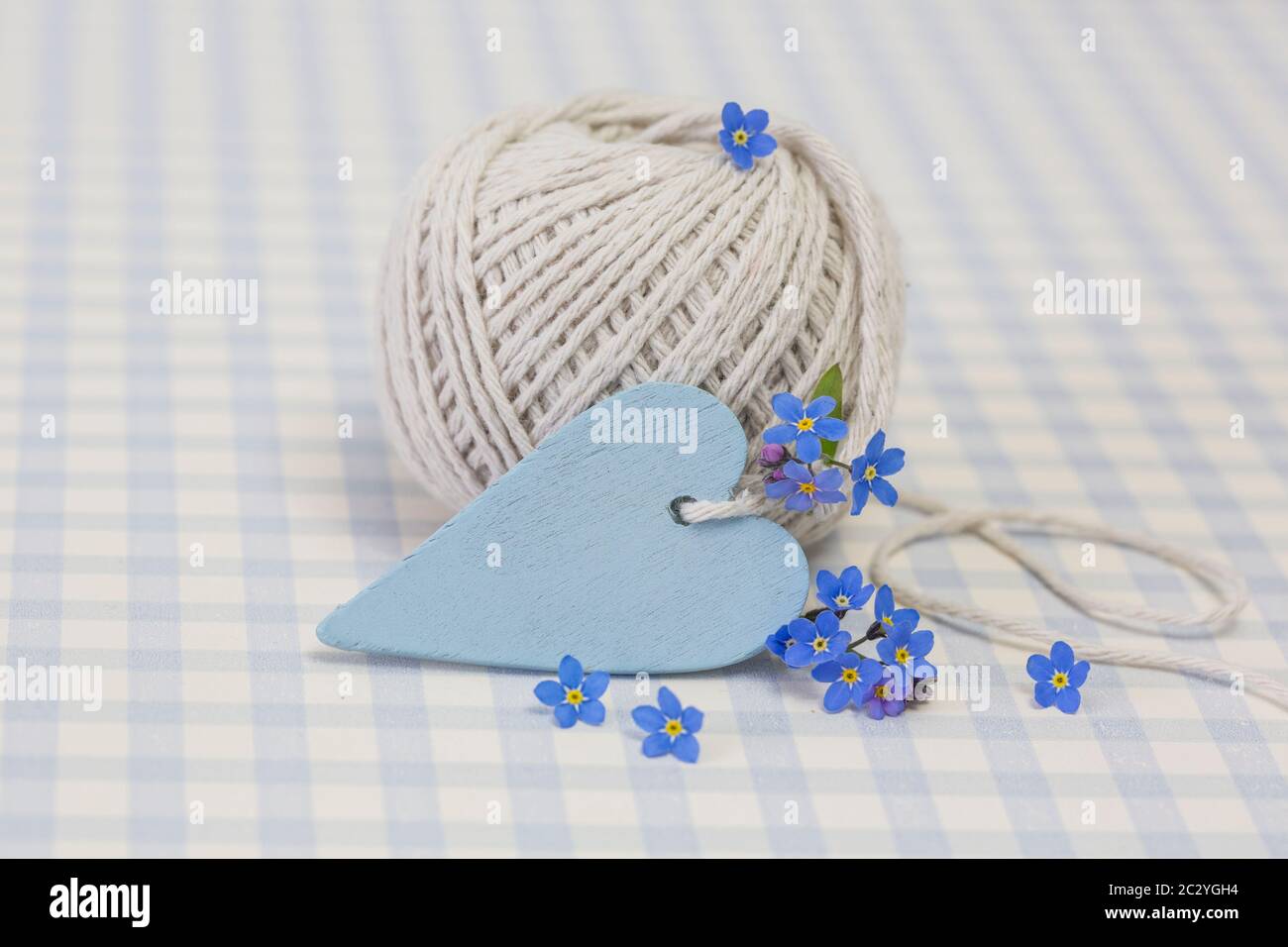 spring still life with little forget me not flowers, heart and a roll of twine in pastel blue colors on a checkered background Stock Photo