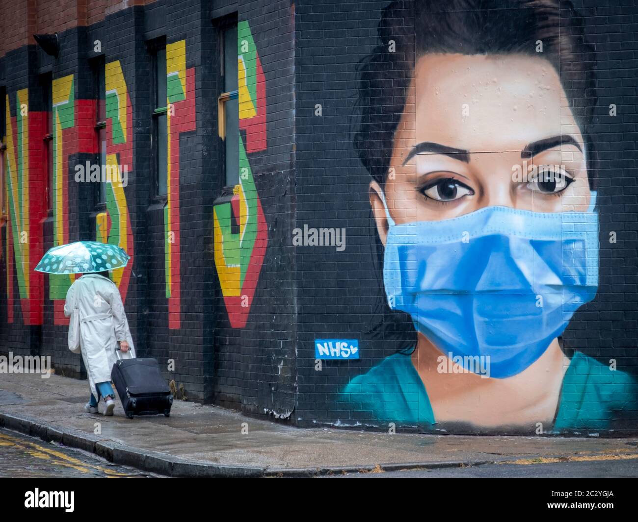 Person walking past face mask graffiti art on London street as the Coronavirus lock down is lifted Stock Photo