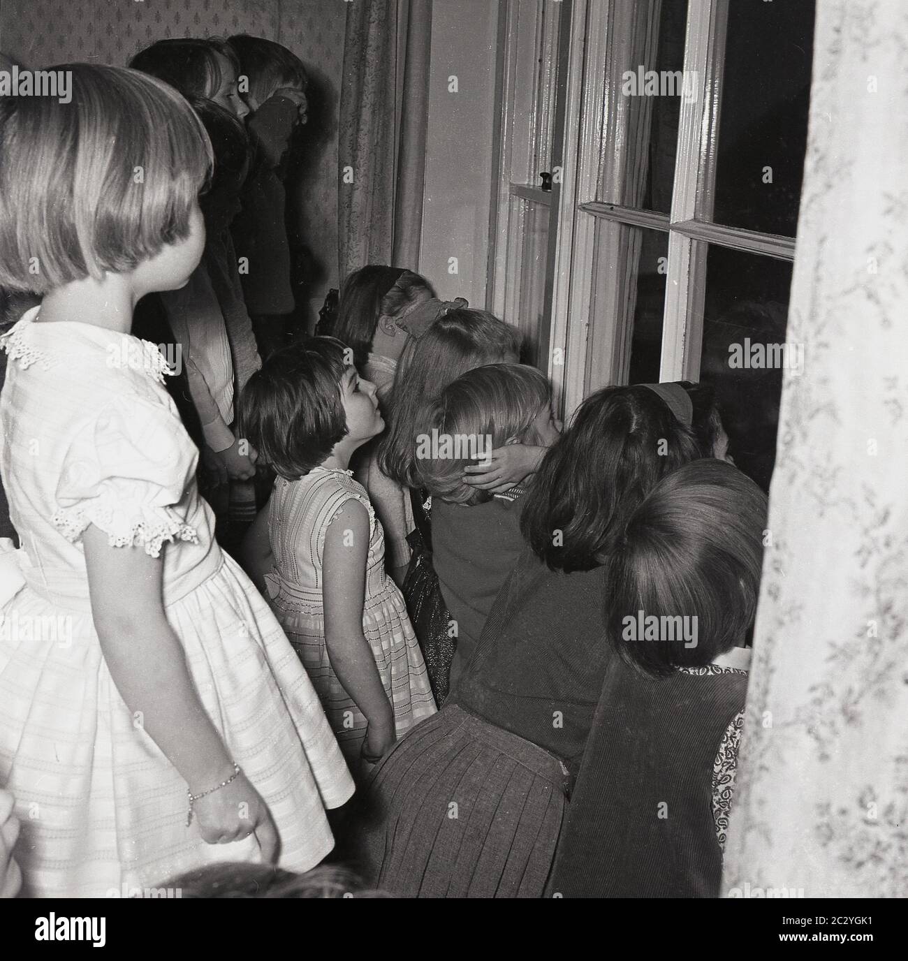 1960s, historical, excited young children at a party in a house peering out the window to see the surprise, England, UK. Stock Photo