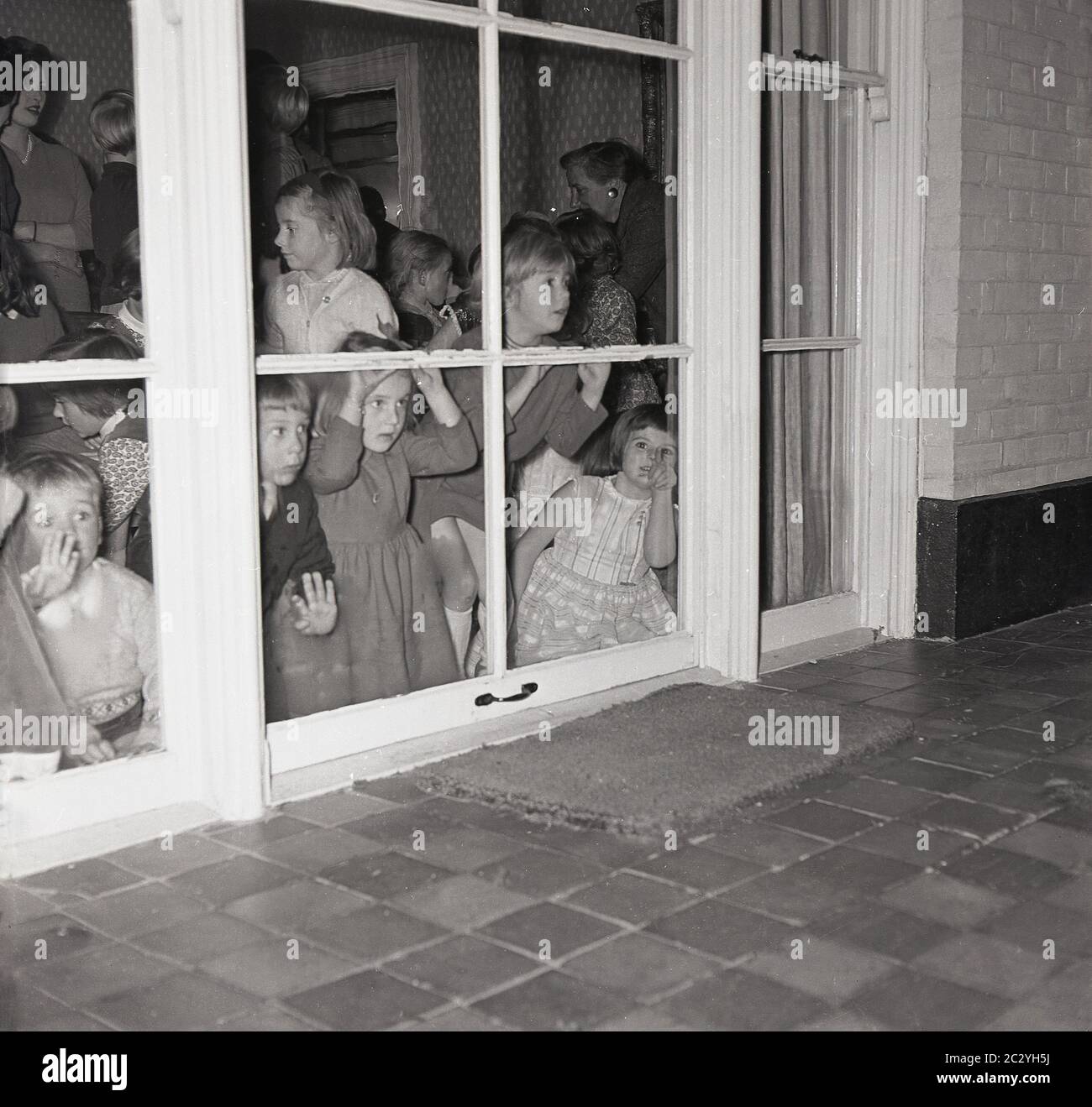 1960s, historical, a grouo of excited young children at a party in a house peering out the windows at the back of house to the patio ouside to try and see the surprise, England, UK. Stock Photo