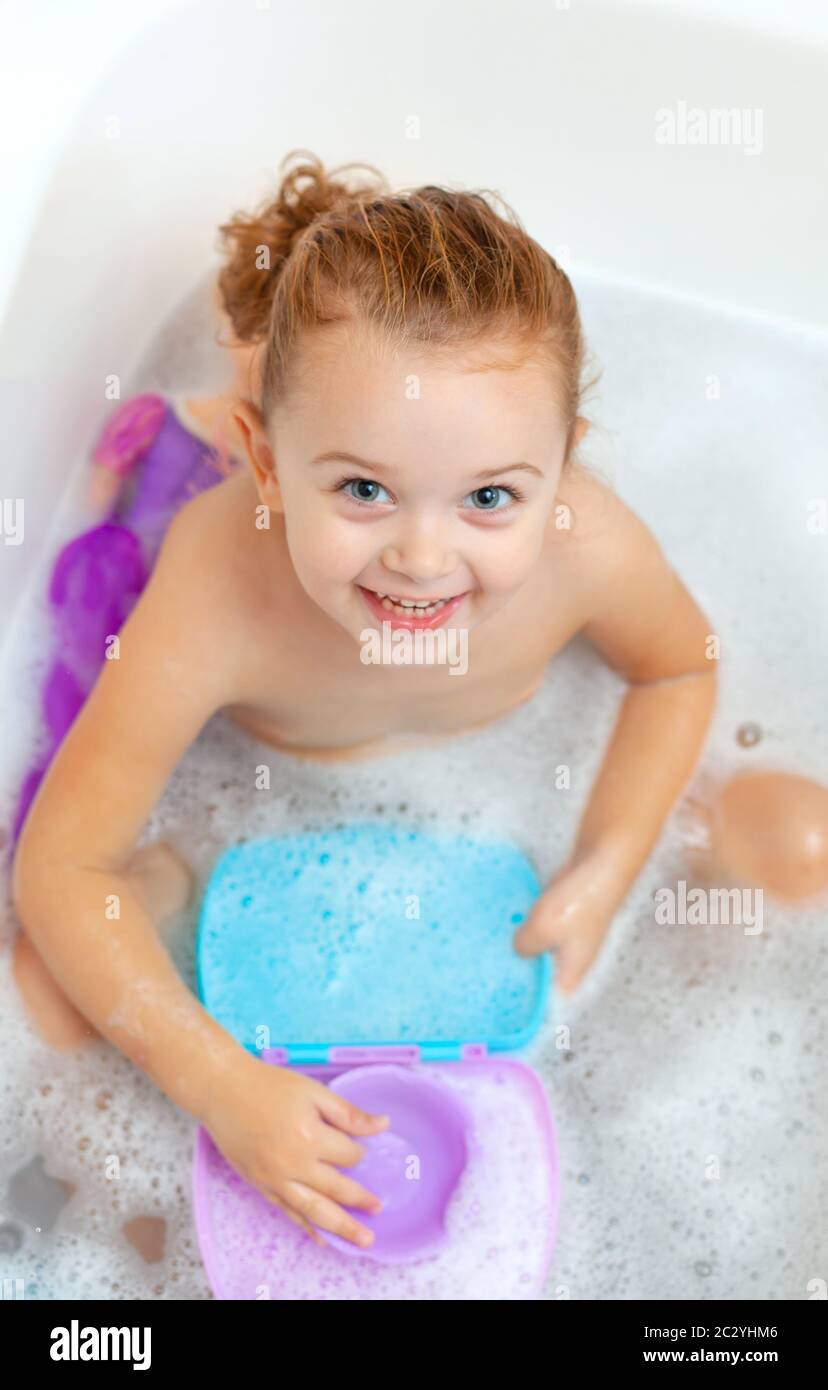 Cute adorable baby girl taking foamy bath in bathtub. Toddler playing