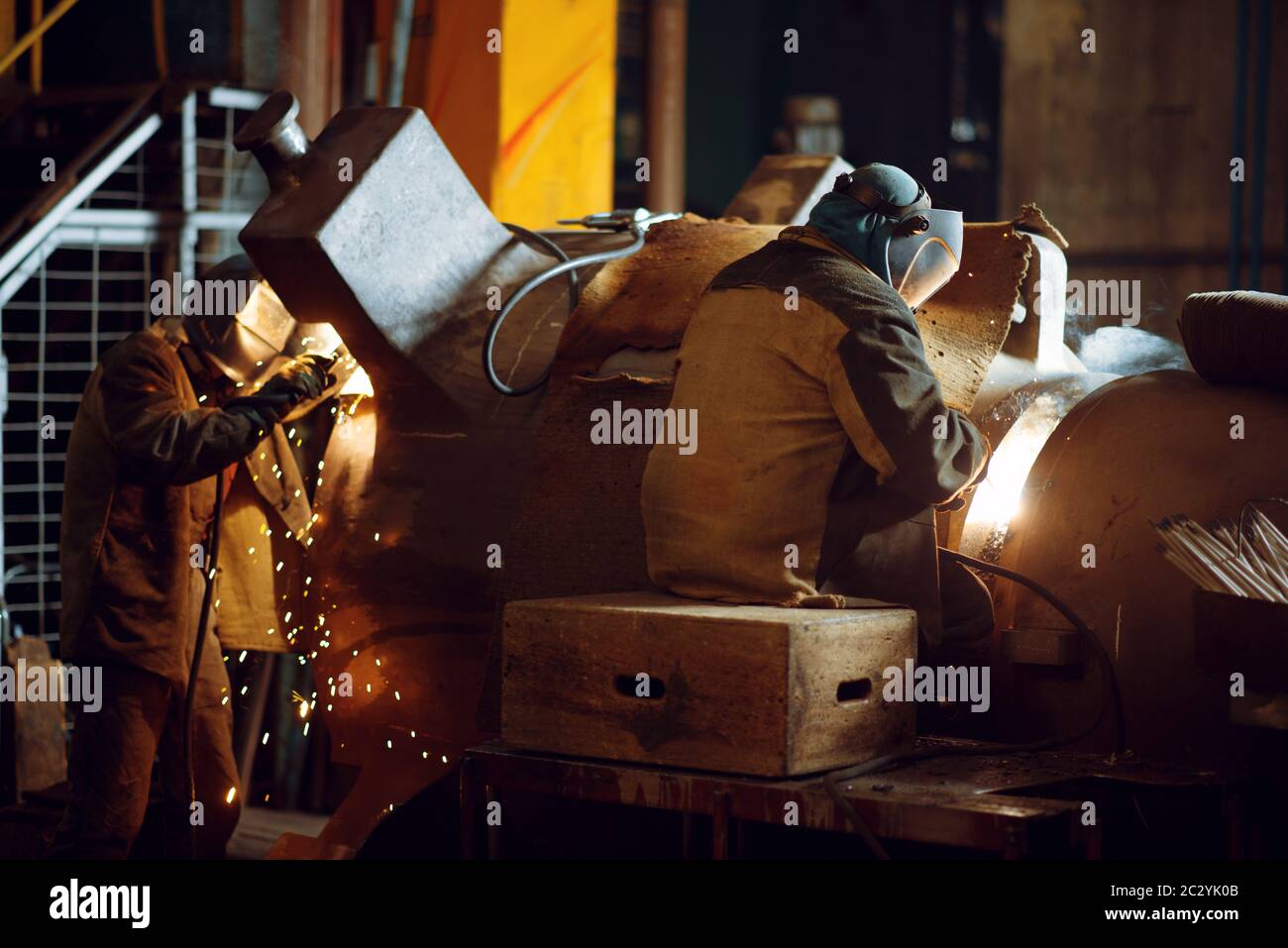 Two welder in masks works with big metal pipe on factory, welding skill