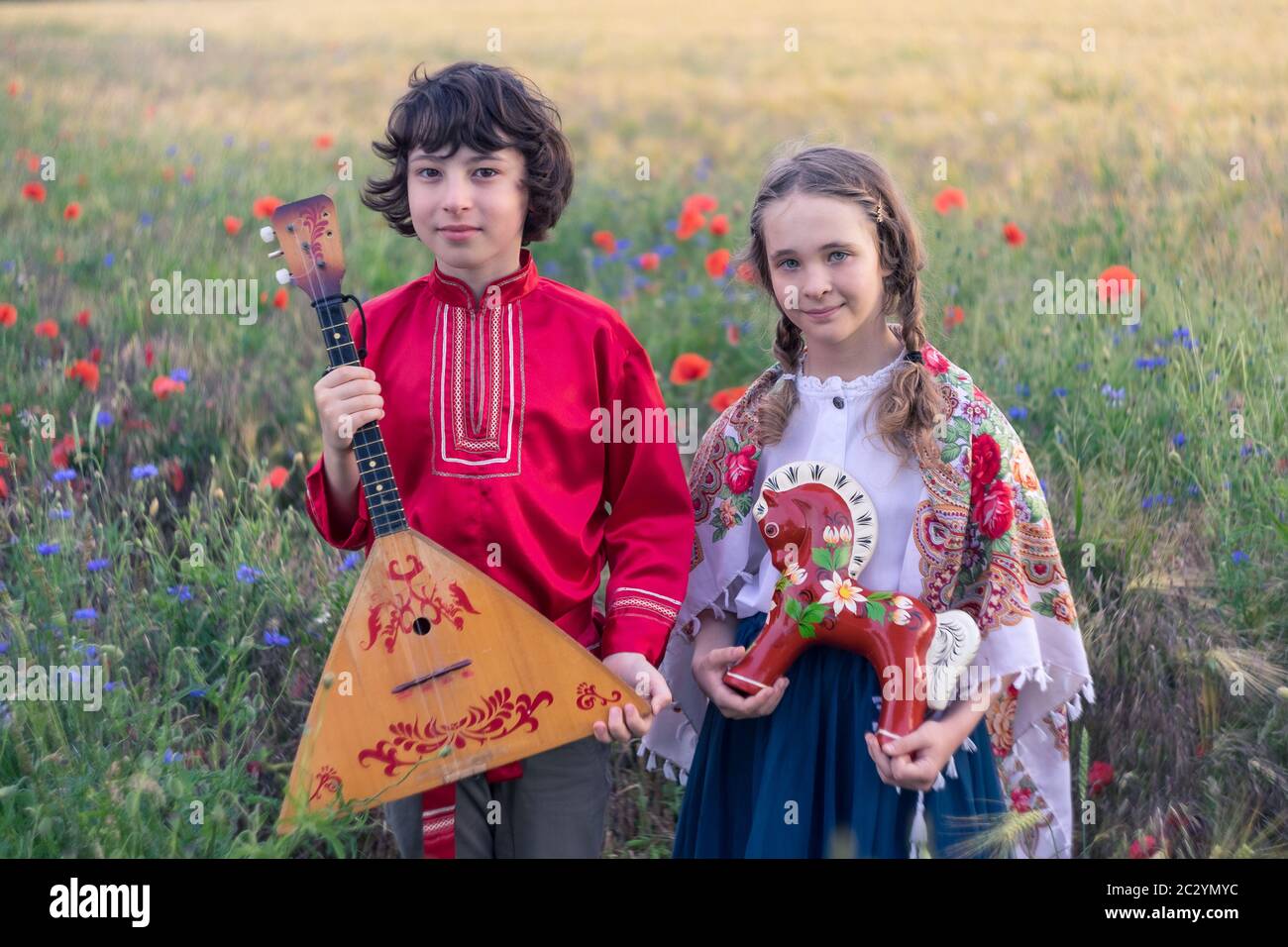 Portrait of a boy and a girl in the field. On the girl is a shawl with folk patterns. In the hands of a wooden horse painted in the style of lubok. Bo Stock Photo
