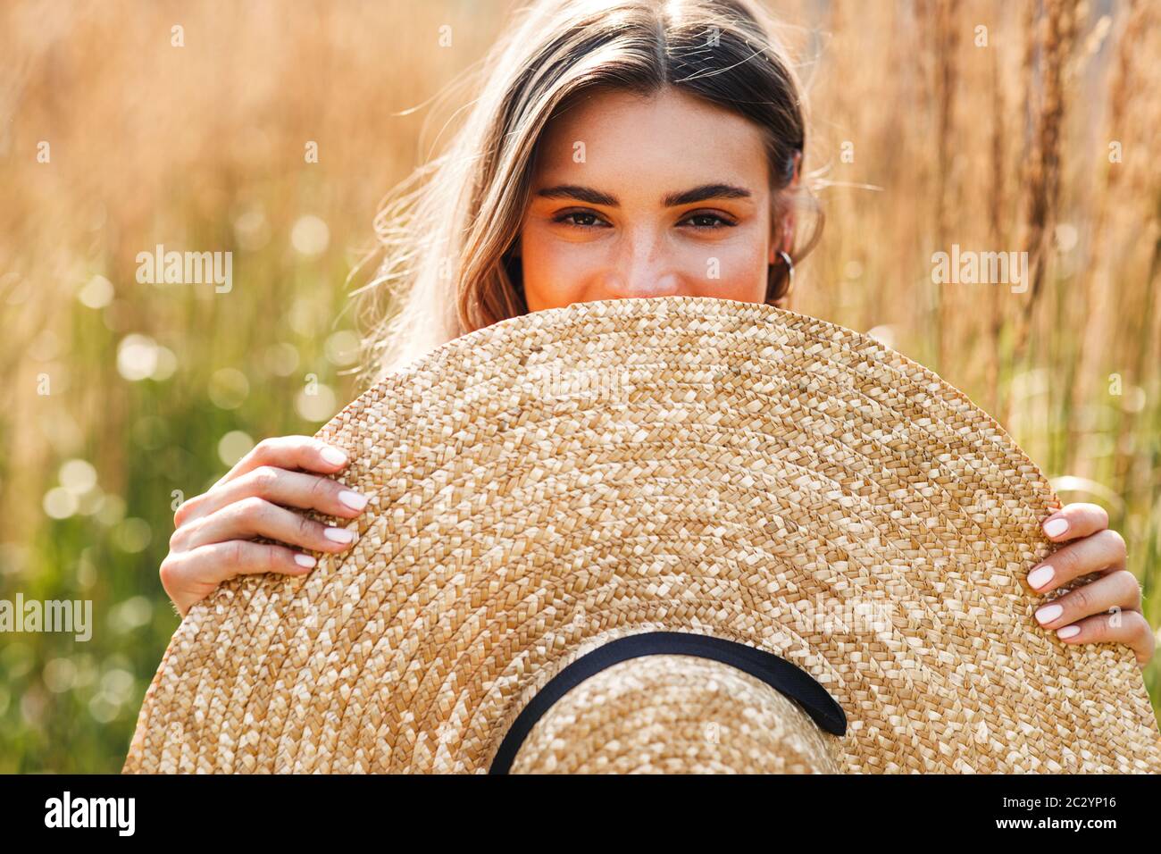 Portrait of beautiful woman peeking through a hat in hand while standing on a field Stock Photo