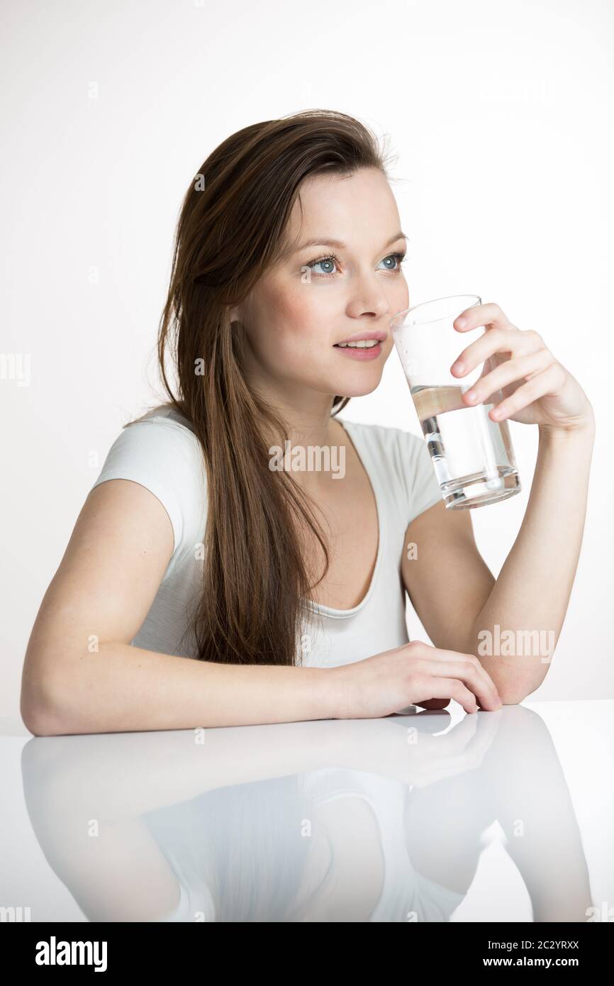 Pretty, young woman in her modern, clean and bright kitchen, pouring herself and drinking a glass of cold tap water(color toned imagey; shallow DOF) Stock Photo