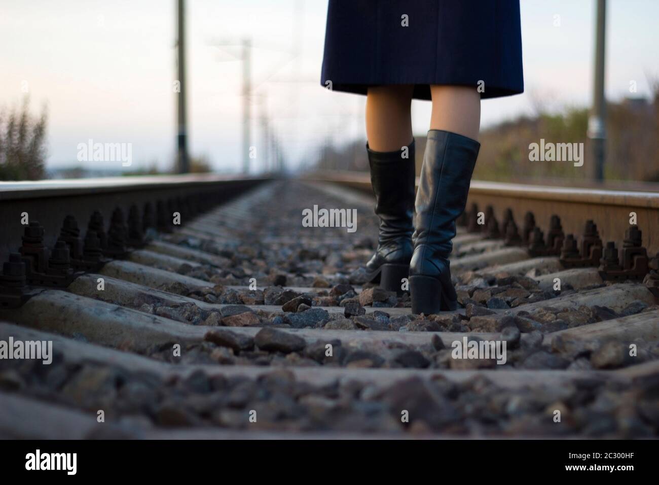 Girl walks on railway rails in a coat and boots - travel, depression, lifestyle Stock Photo