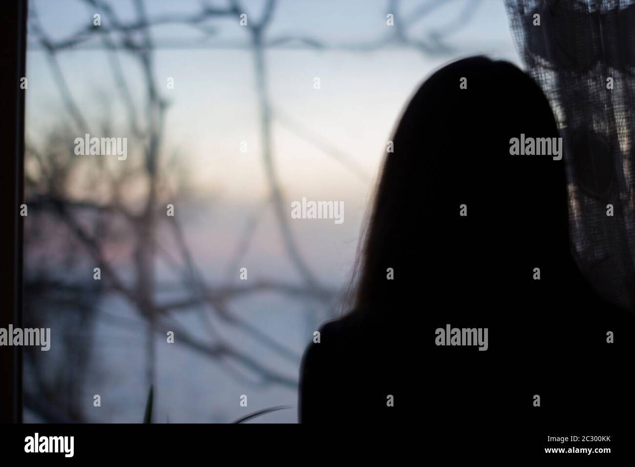 Silhouette of a girl on a background of a dark window in the house - depression, reflection, danger, blur Stock Photo