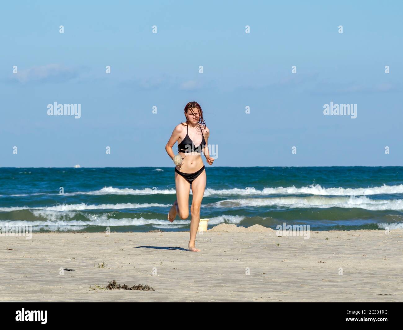 A young Caucasian girl in a black bikini bathing suit runs on the beach in Port Aransas, Texas USA. Stock Photo