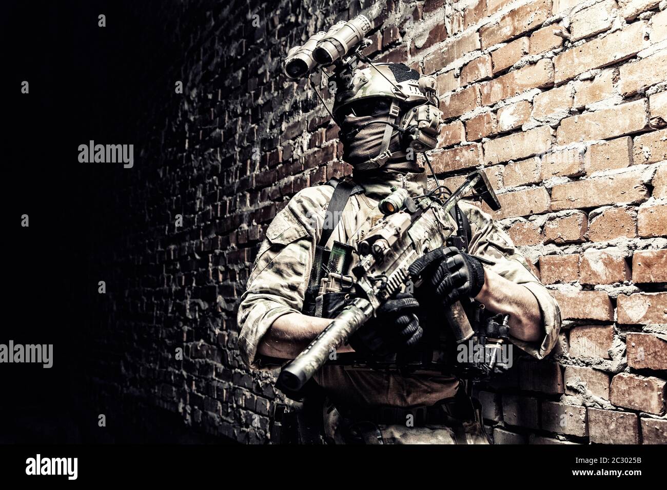 Special operations forces soldier, counter terrorism assault team fighter with night vision device on helmet and service rifle, low key indoor shot br Stock Photo