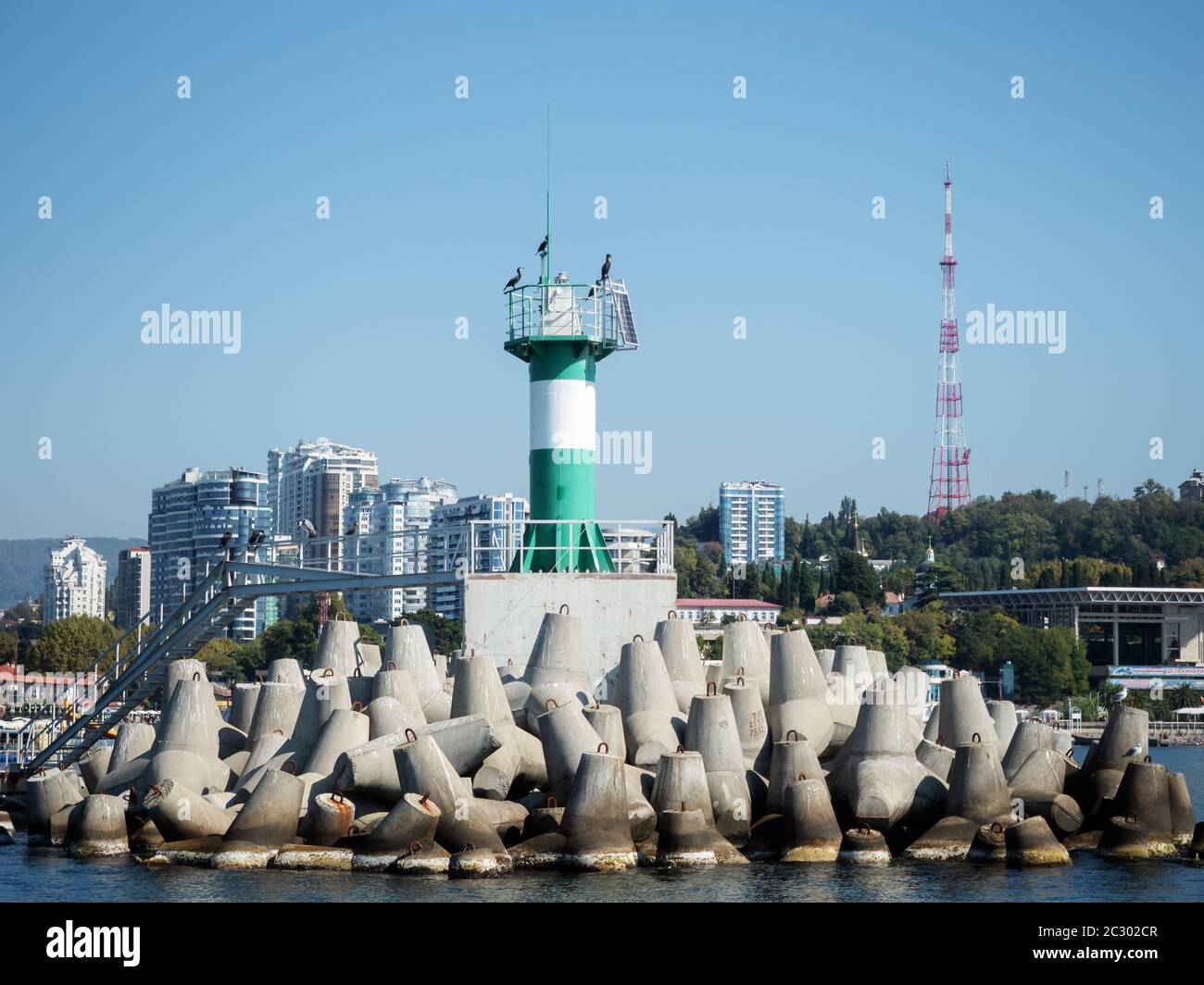 Green lighthouse with birds on a pier in the sea Stock Photo
