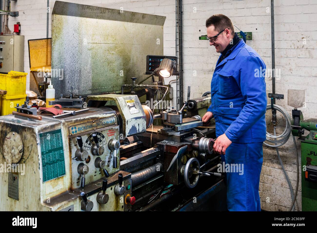 A worker in blue overall is working at a lathe machine Stock Photo