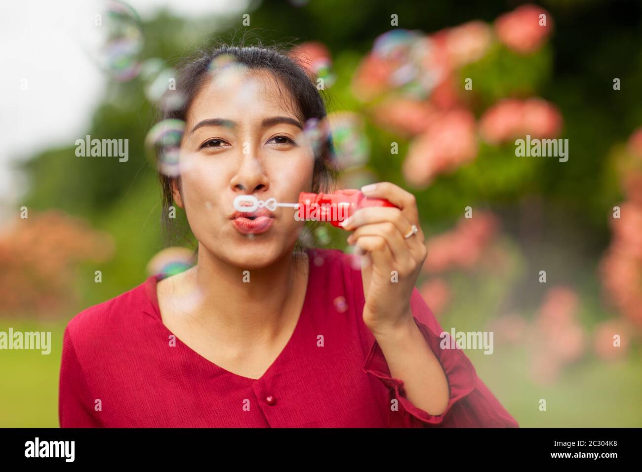 Portrait of beautiful young asian woman with Carmen red dress blowing bubble in the park Stock Photo