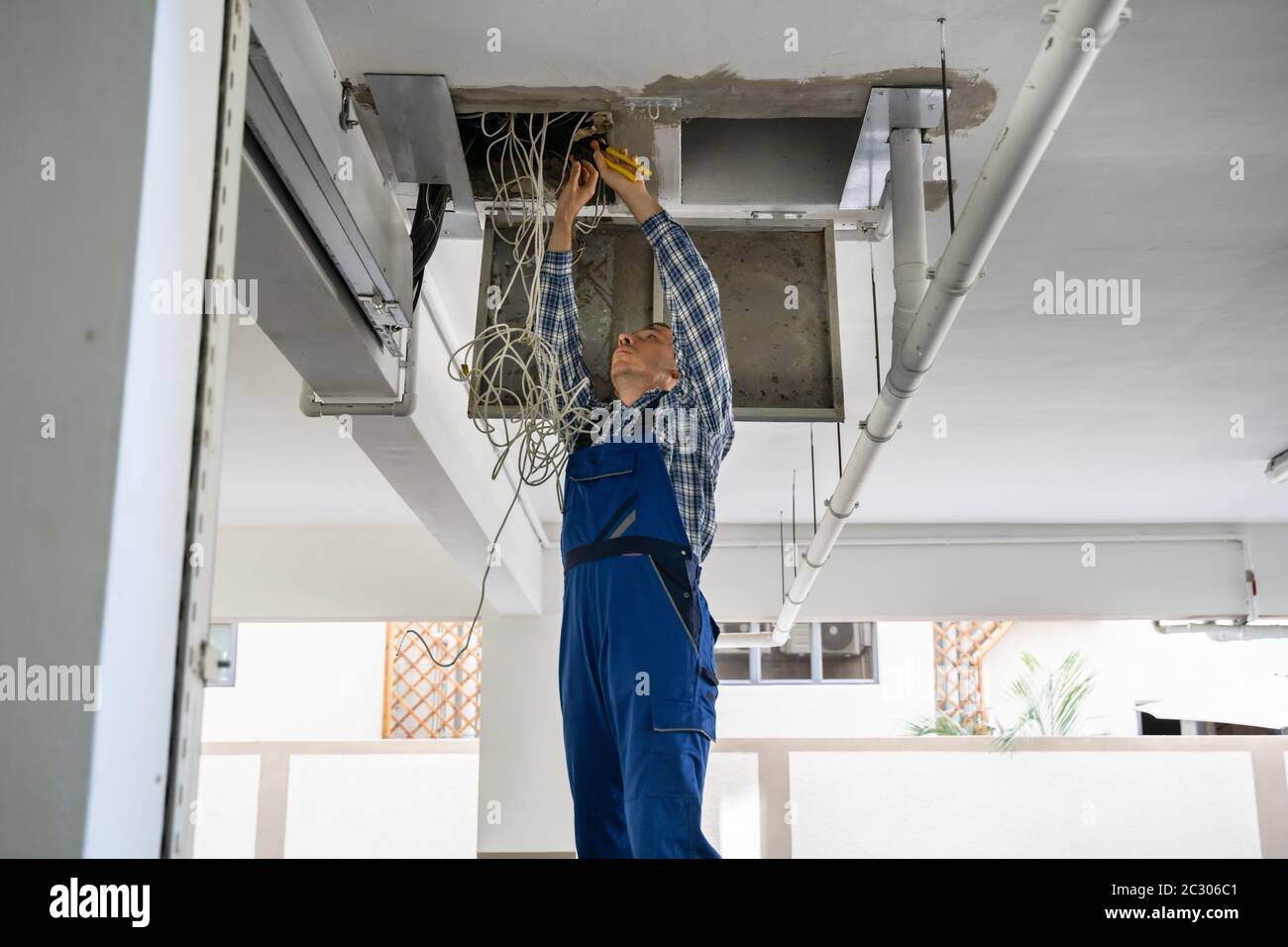 Male Electrician On Step Ladder Installing Light At Corridor Stock