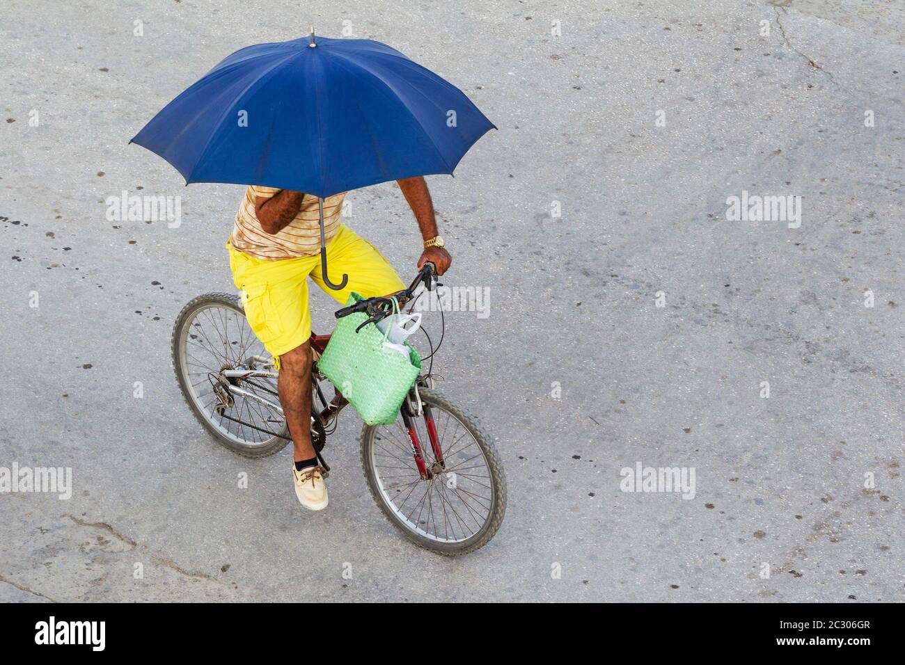 Cyclist using an umbrella as sunshade, Niquero, Cuba Stock Photo
