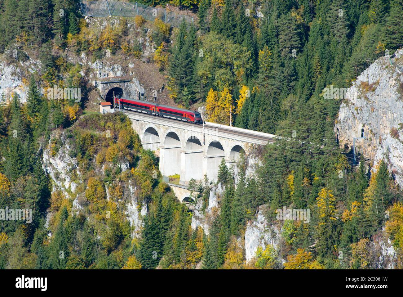 Red train on a viaduct between two tunnels on the Semmering Railway