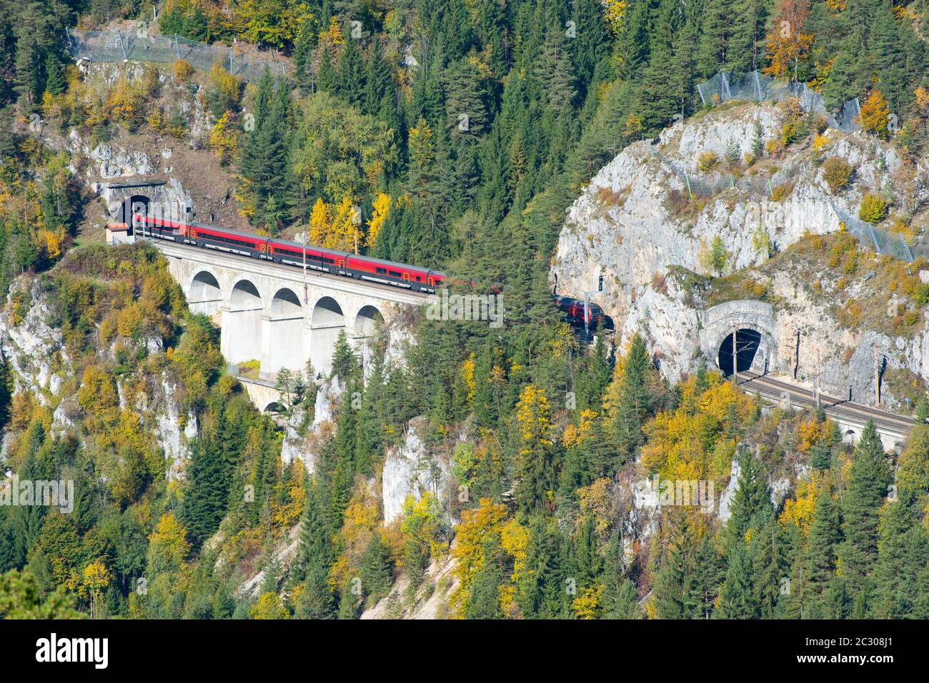 Red train on a viaduct between two tunnels on the Semmering Railway