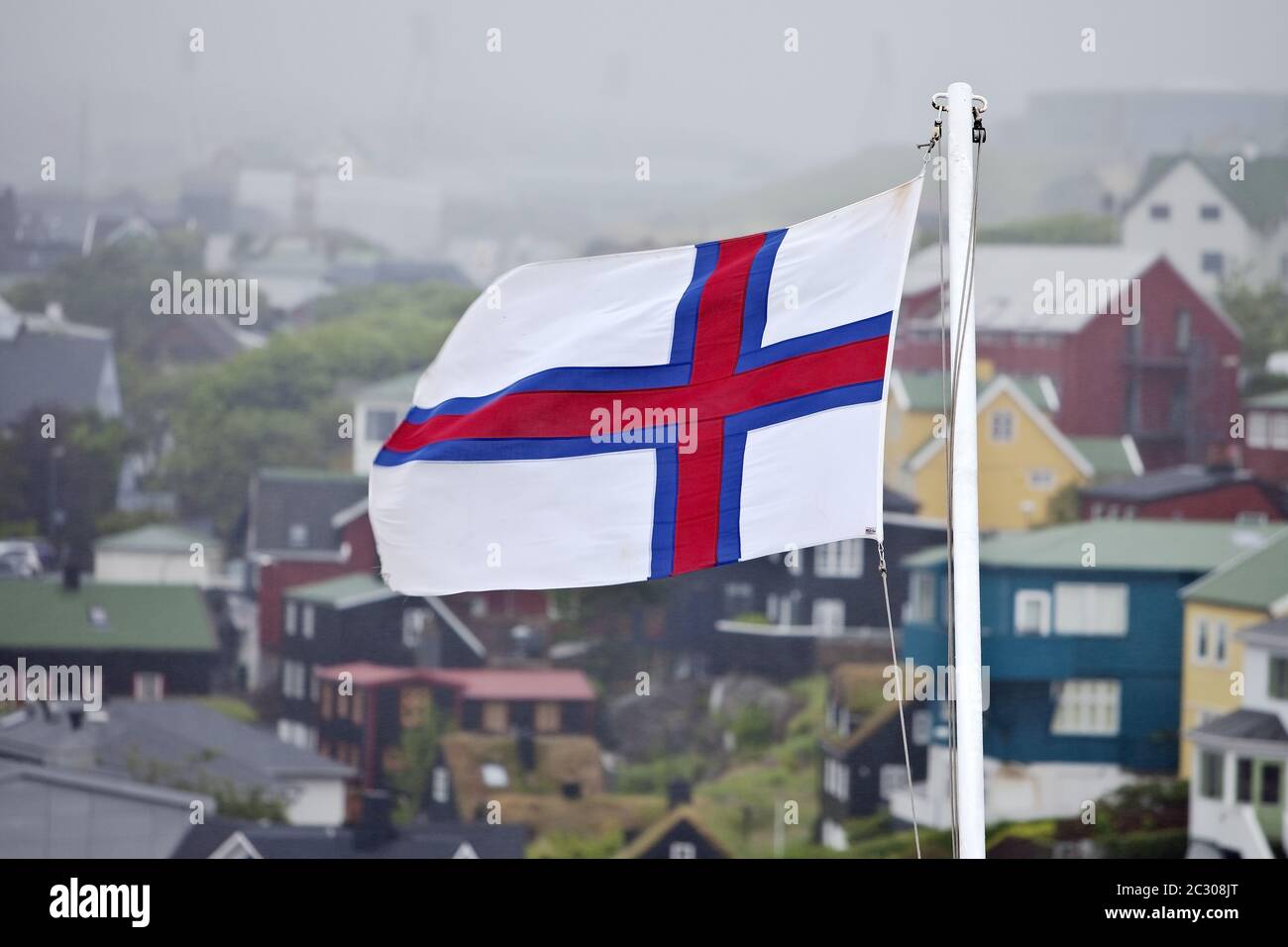 Flag of Faeroeer in front of houses in the fog, Thórshavn, Faeroeer, Føroyar, Denmark, Europe Stock Photo