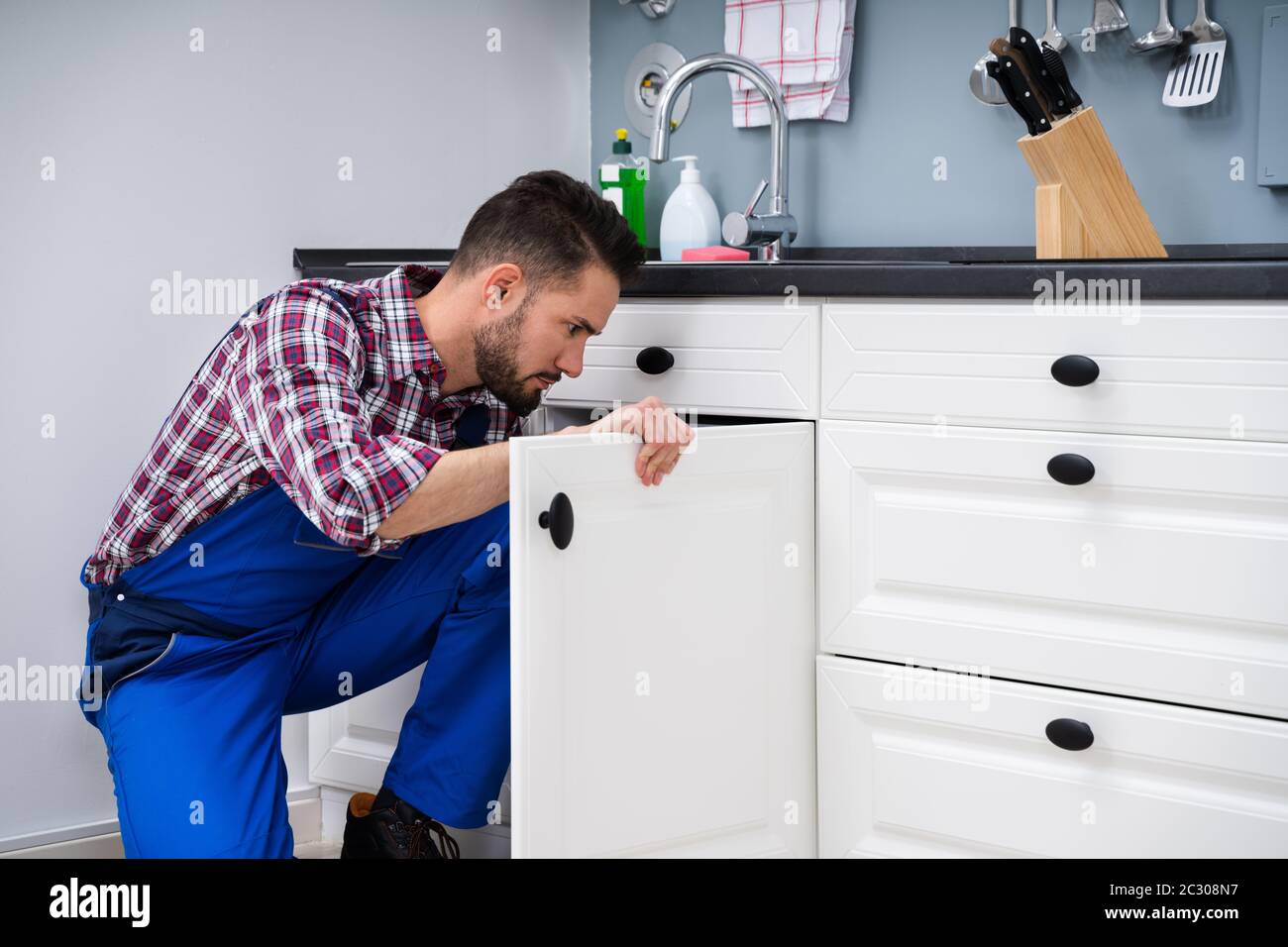Young Handyman Fixing Sink Door In Kitchen Stock Photo