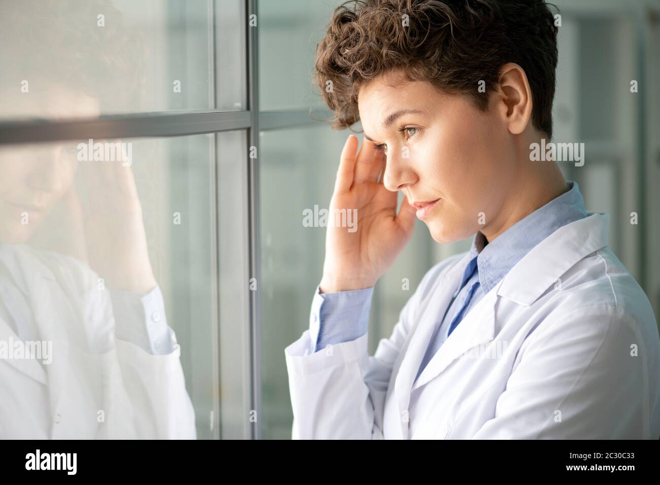 Tired female lab worker with short hair standing at window of
