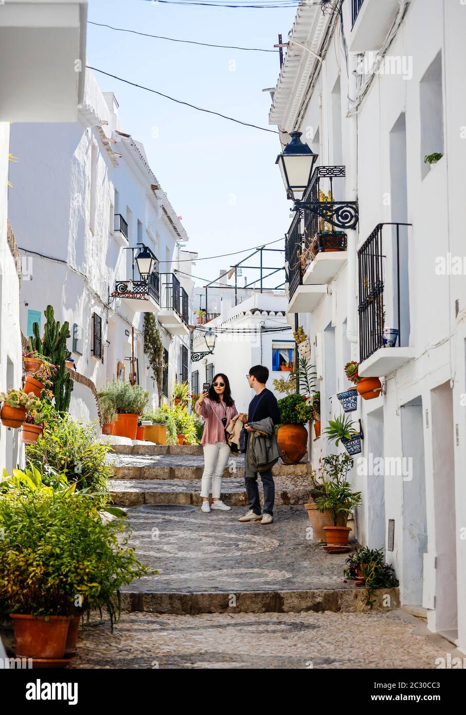 Asian tourists take pictures of themselves in picturesque alleys in the white mountain village of Frigiliana, Frigiliana, province of Malaga Stock Photo