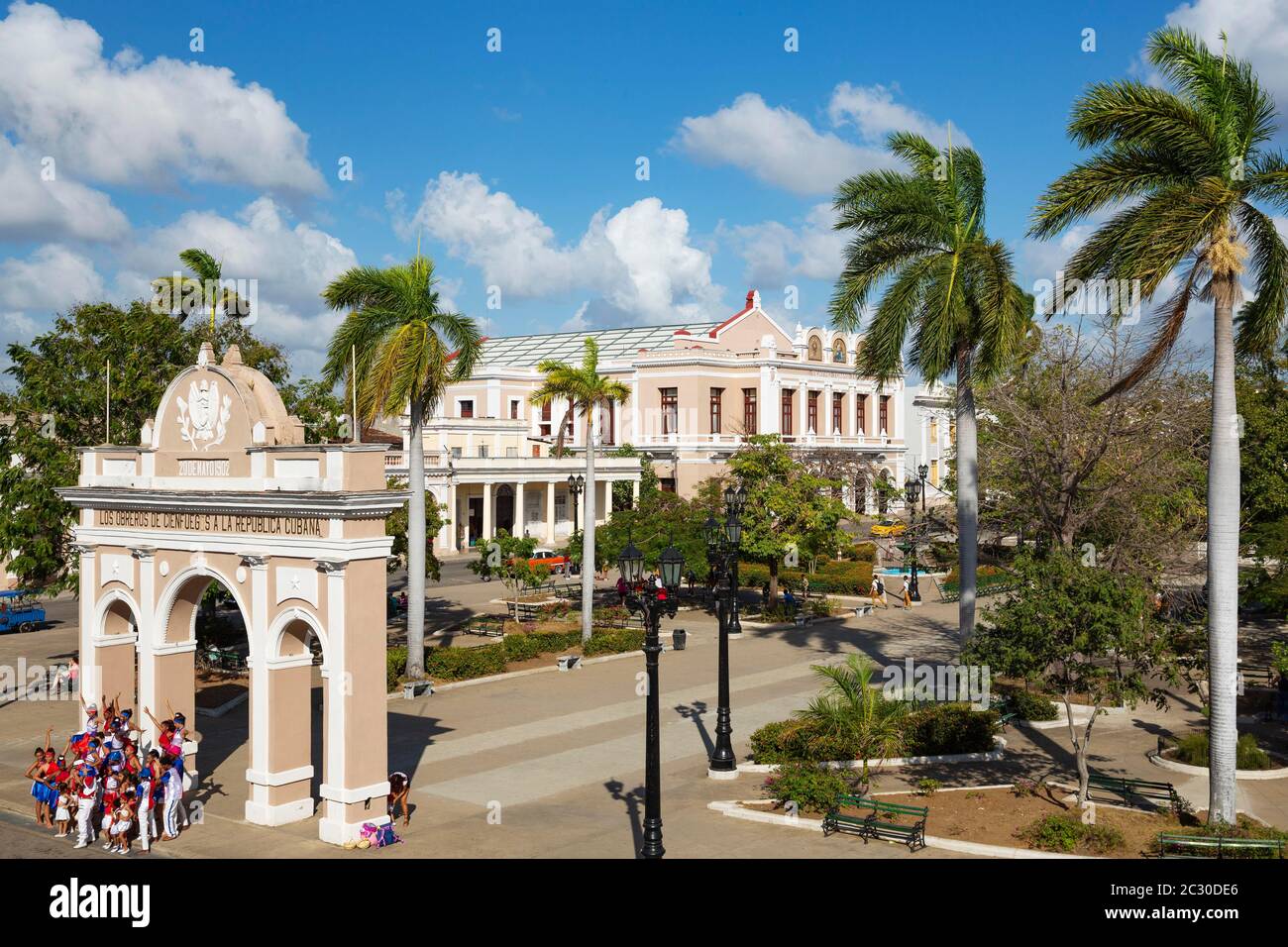 Porticoed Neoclassical buildings frame the Parque Jose Marti, bottom left a dancing chorus poses for a photo., Cienfuegos, Cuba Stock Photo
