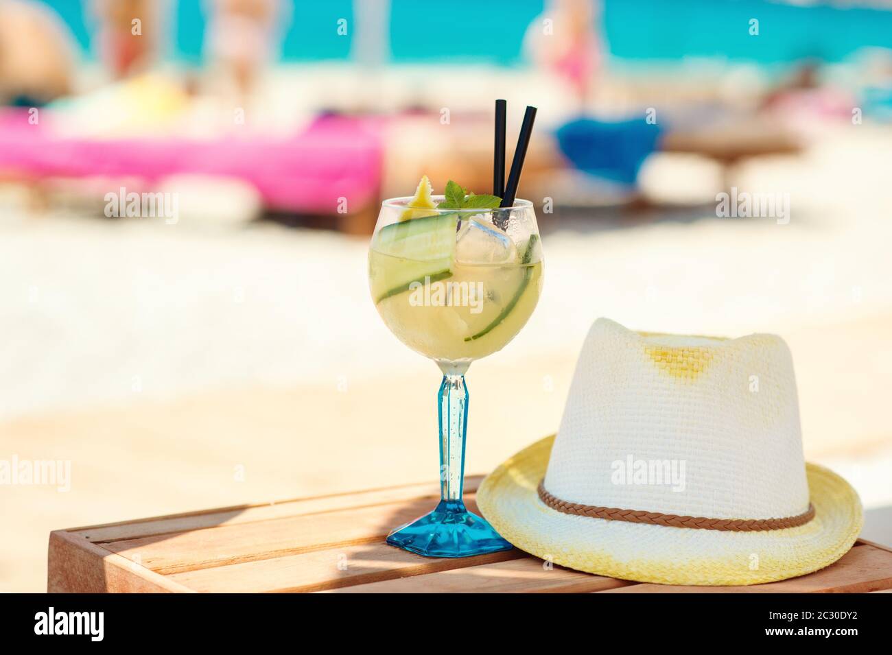 Cucumber drink cocktail, straw hat on wooden table on sandy beach with turquois water sea shore Stock Photo