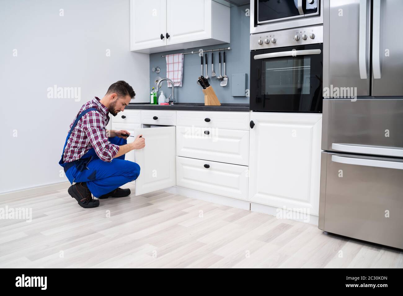 Young Handyman Fixing Sink Door In Kitchen Stock Photo