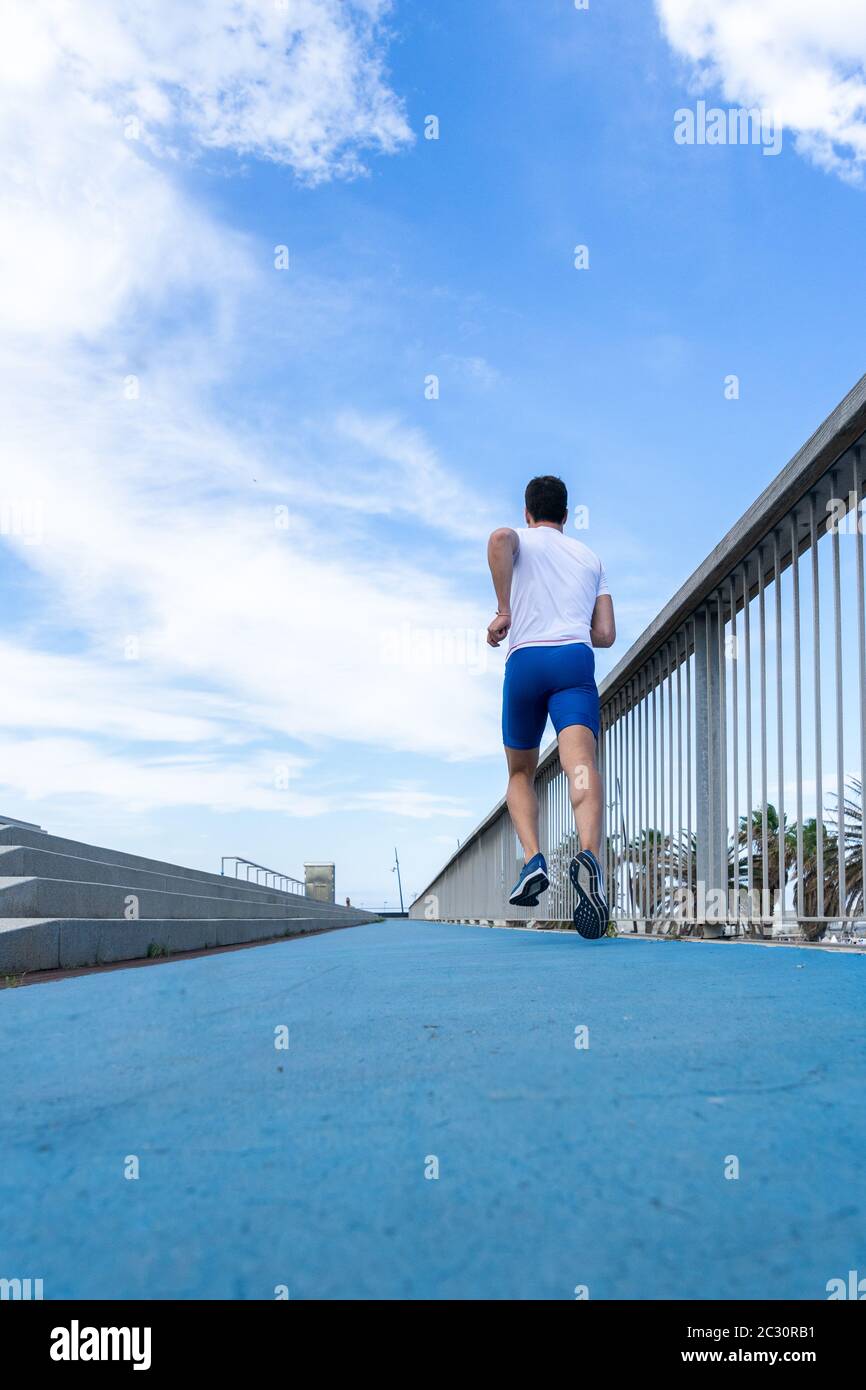 Young runner man in blue pants and white t-shirt running in the sun on a blue track. Motivation concept, career Stock Photo