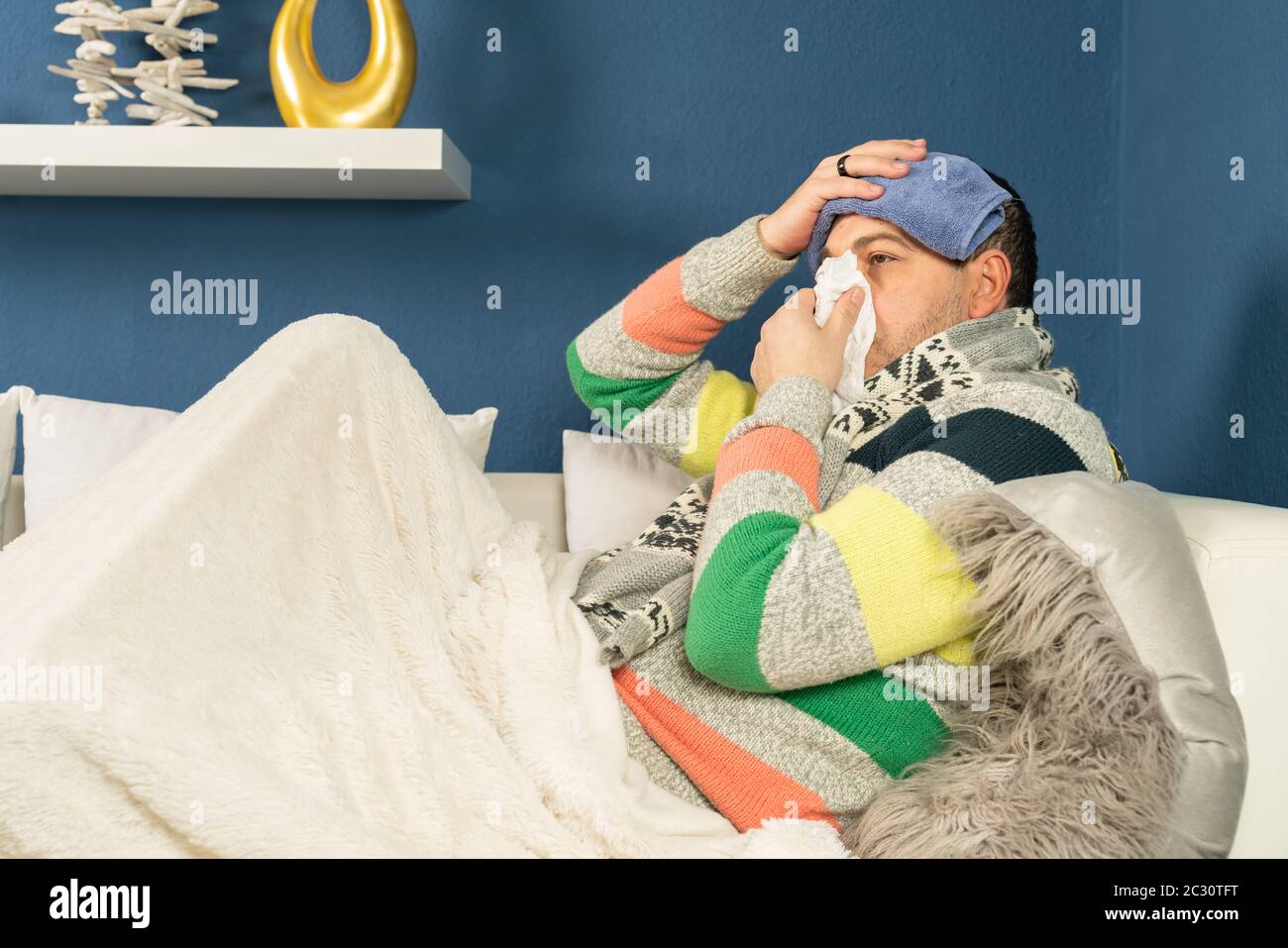 A sick man with a rag on his head and a handkerchief in his hand is lying on his couch Stock Photo