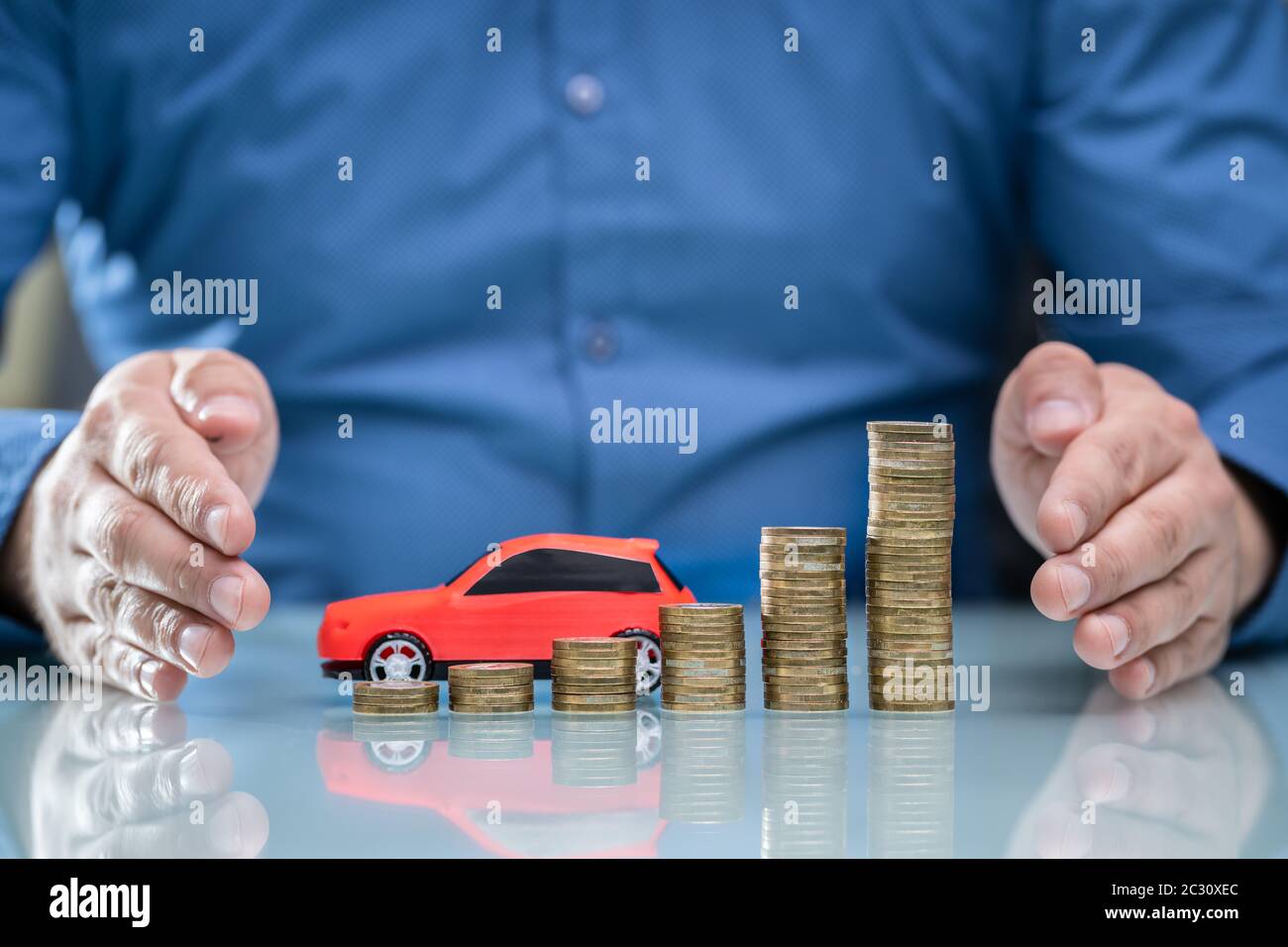 Businessman's Hand Protecting Growing Stacked Coins And Red Car On Desk Stock Photo