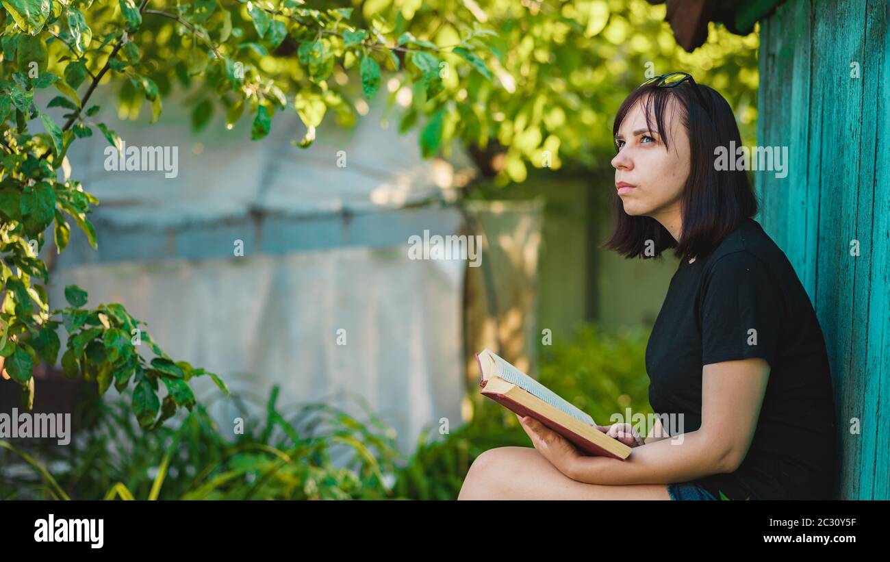 Close up of young woman with book in garden. Female resting in nature, enjoying her leisure time. Stock Photo