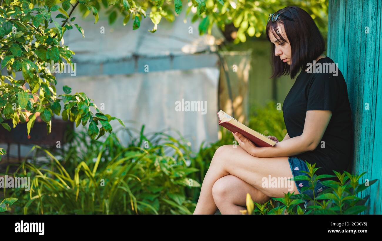 Close up of young woman reading book in garden. Female resting in nature, enjoying her leisure time. Stock Photo