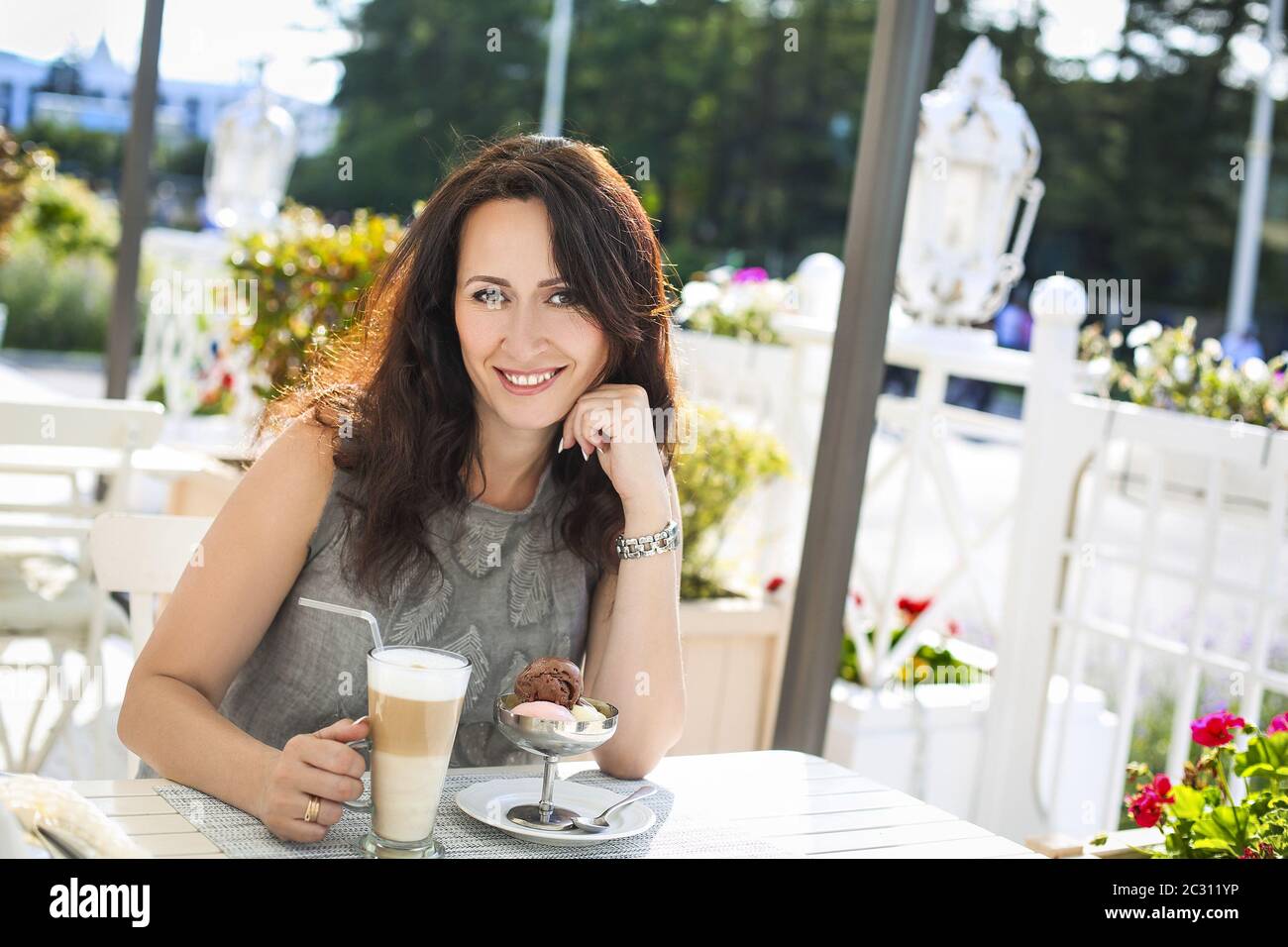 Woman drinking latte coffee and eating ice cream in outdoor cafe Stock Photo
